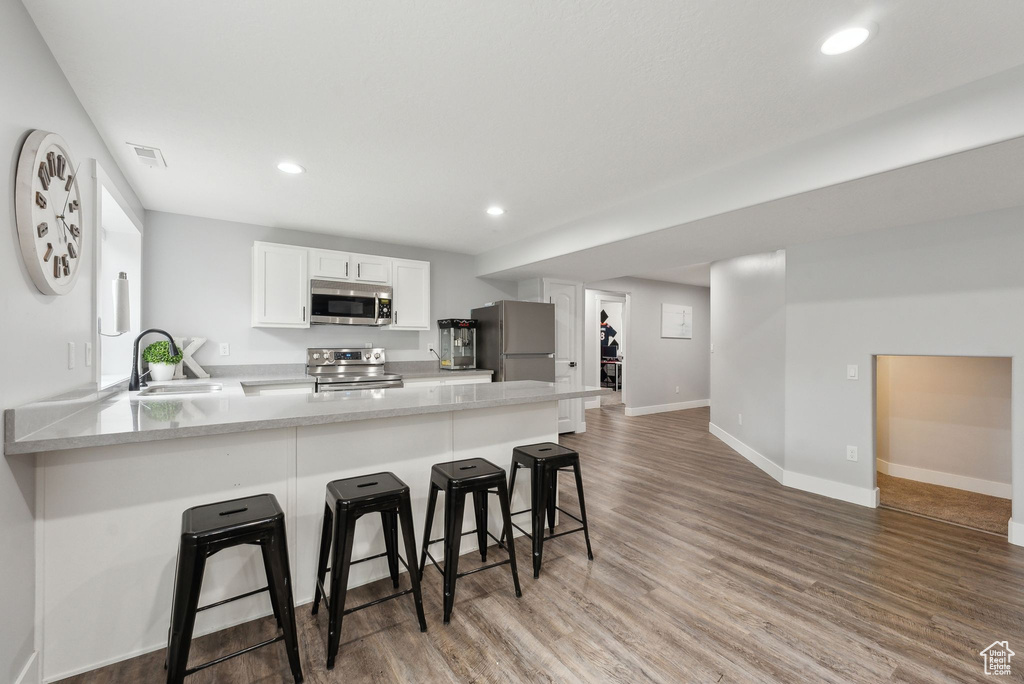 Kitchen with stainless steel appliances, a sink, a peninsula, light wood finished floors, and a breakfast bar