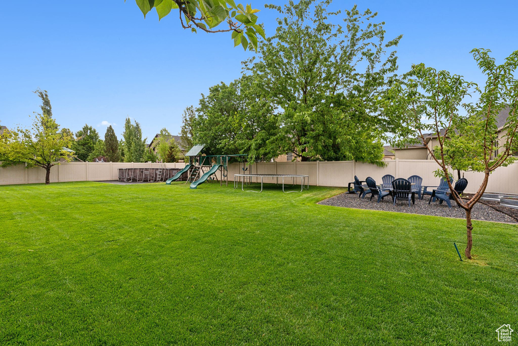 View of yard featuring a playground, a trampoline, and an outdoor fire pit