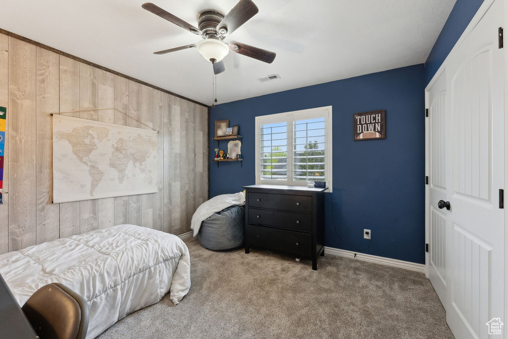 Carpeted bedroom with wood walls, baseboards, and ceiling fan