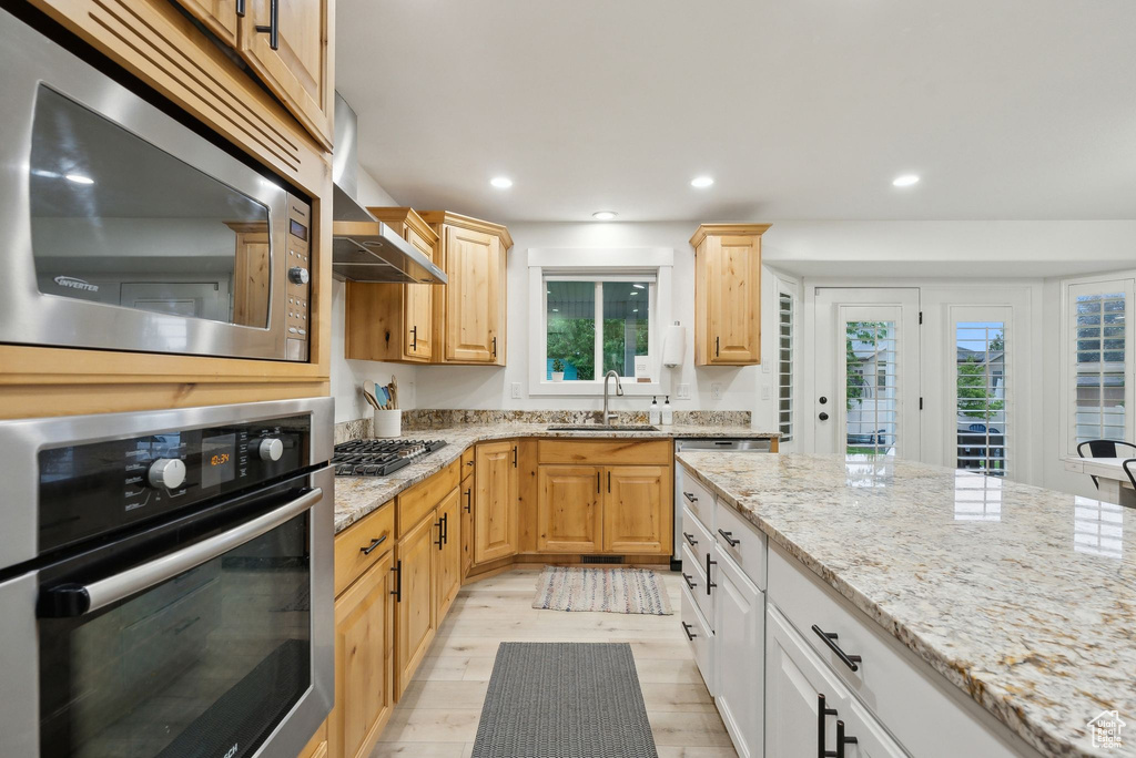 Kitchen featuring appliances with stainless steel finishes, a sink, light stone counters, light brown cabinets, and light wood finished floors