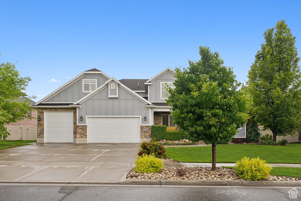 Craftsman-style house with board and batten siding, concrete driveway, a front yard, stone siding, and a garage
