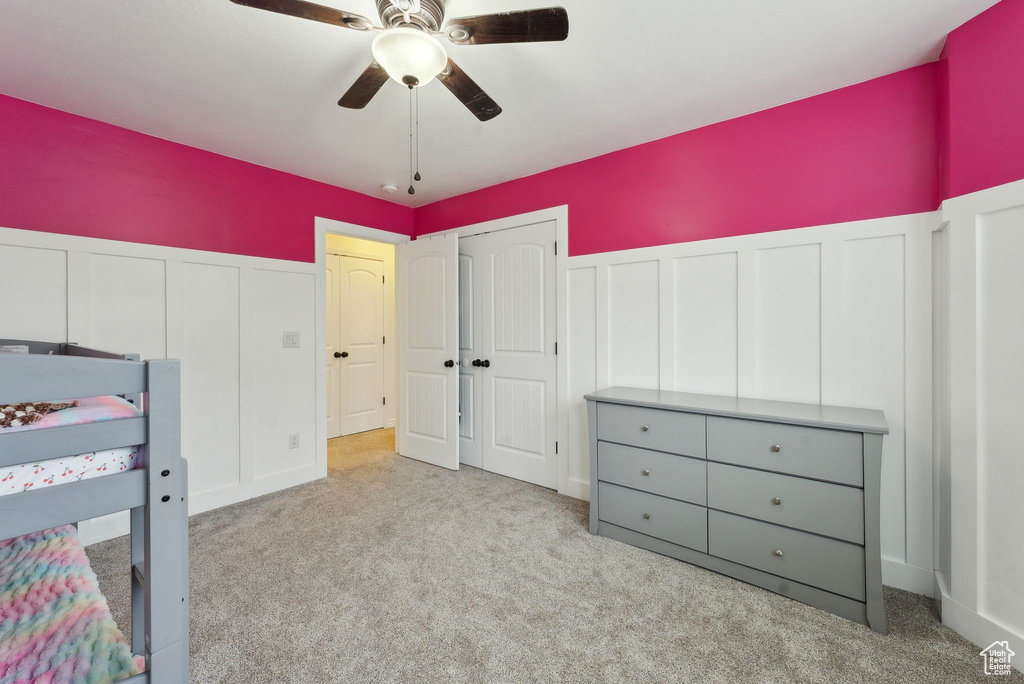 Unfurnished bedroom featuring a decorative wall, carpet floors, wainscoting, ceiling fan, and a closet