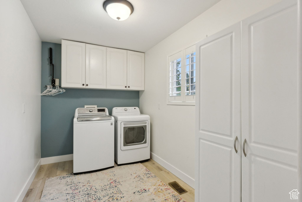 Laundry area with cabinet space, washer and dryer, light wood-style floors, and baseboards