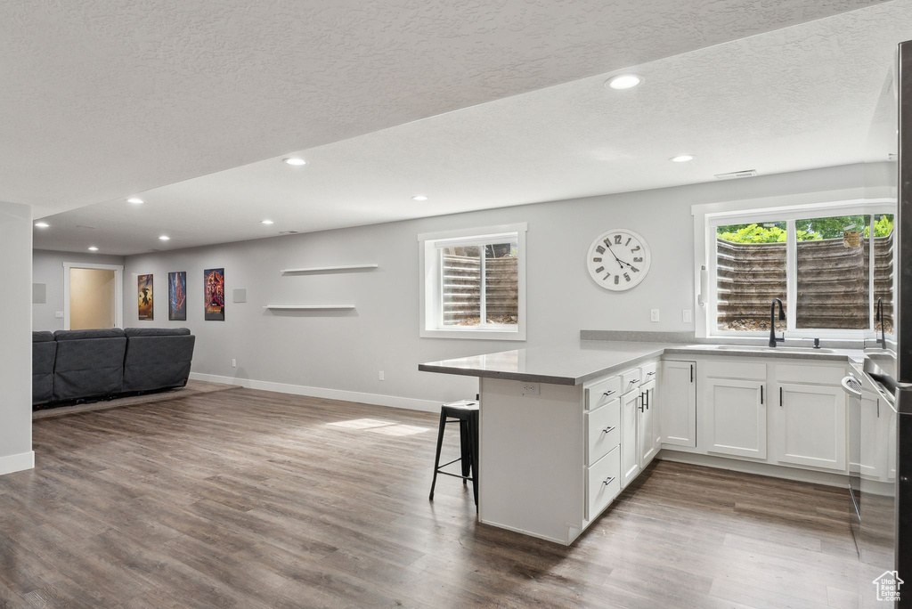 Kitchen featuring a sink, open floor plan, a peninsula, baseboards, and a kitchen bar