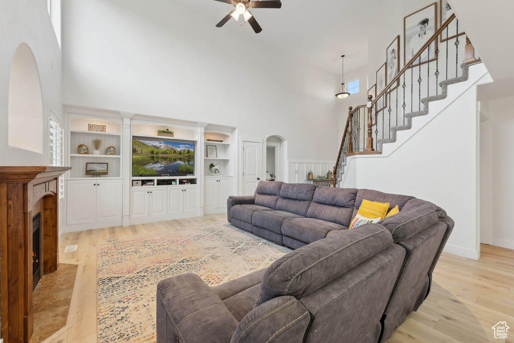 Living area with a towering ceiling, arched walkways, ceiling fan, light wood finished floors, and stairs