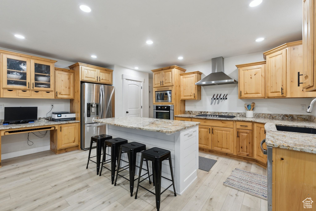 Kitchen featuring stainless steel appliances, a sink, wall chimney exhaust hood, a breakfast bar, and light wood-style floors