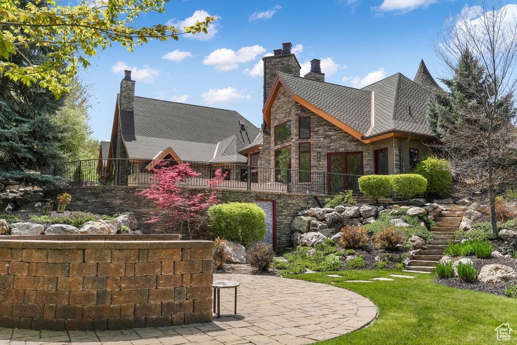View of home\'s exterior featuring stairway, a chimney, a patio, a yard, and stone siding