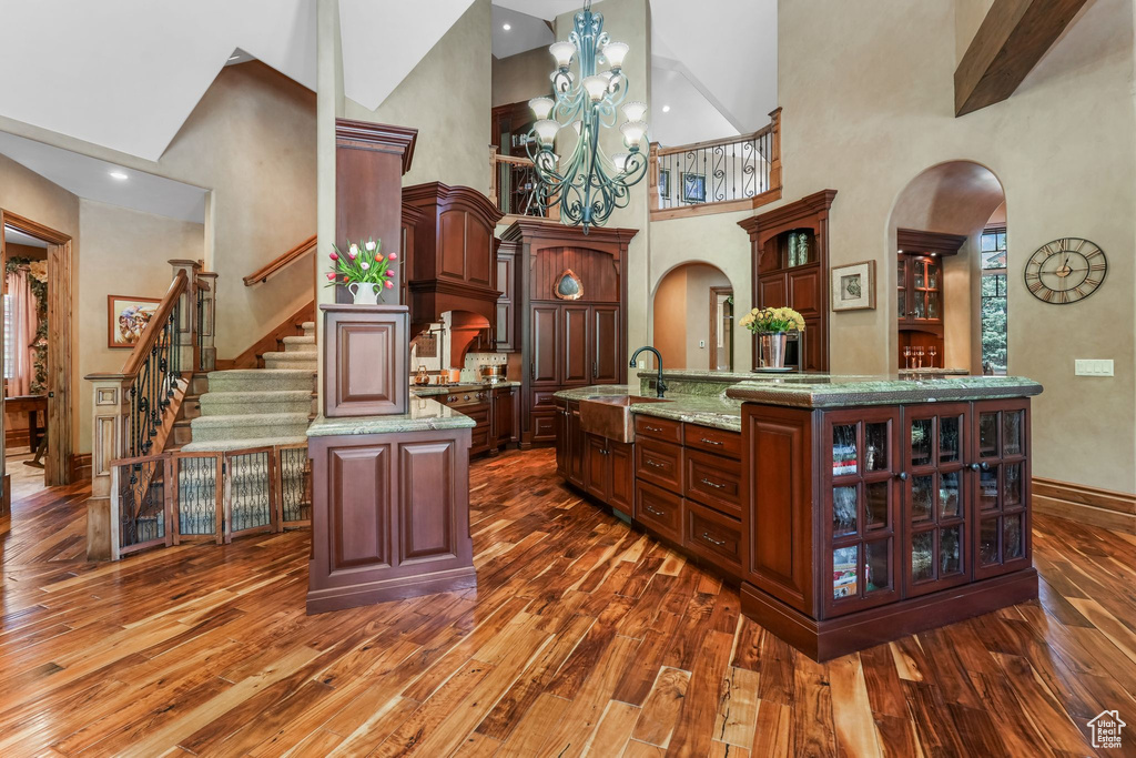 Bar with arched walkways, dark wood-style flooring, high vaulted ceiling, baseboards, and a sink