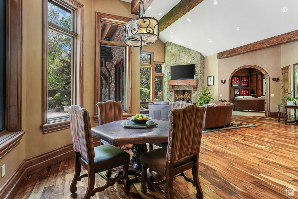 Dining area featuring beam ceiling, baseboards, high vaulted ceiling, hardwood / wood-style floors, and a fireplace