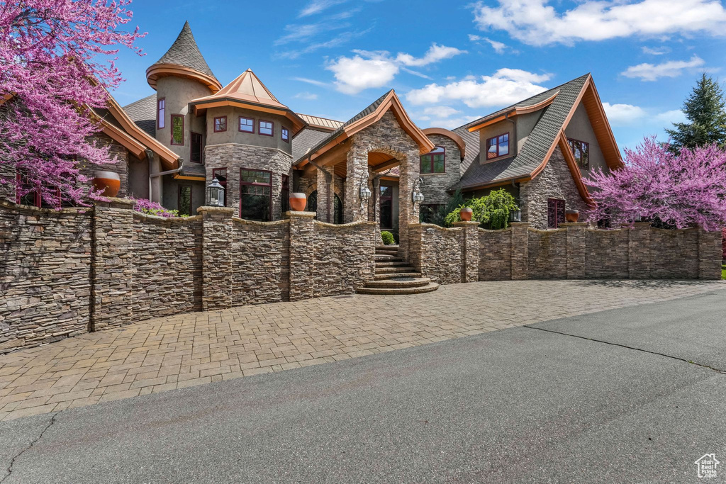 View of front facade featuring stone siding, fence, and stucco siding