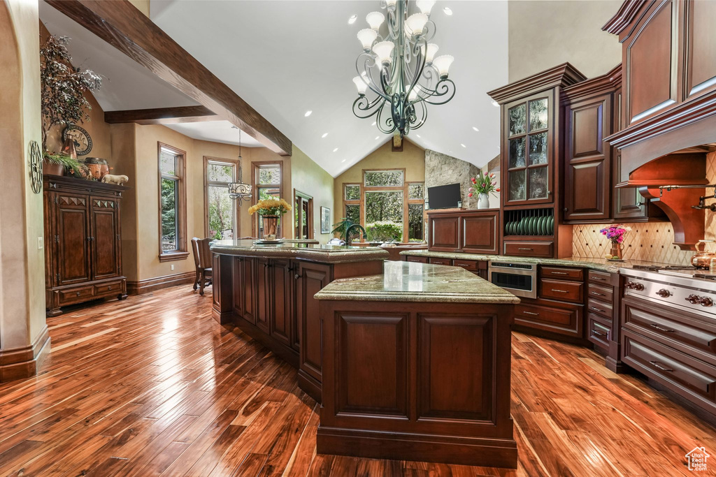 Kitchen with a chandelier, an island with sink, dark wood-style floors, decorative light fixtures, and glass insert cabinets