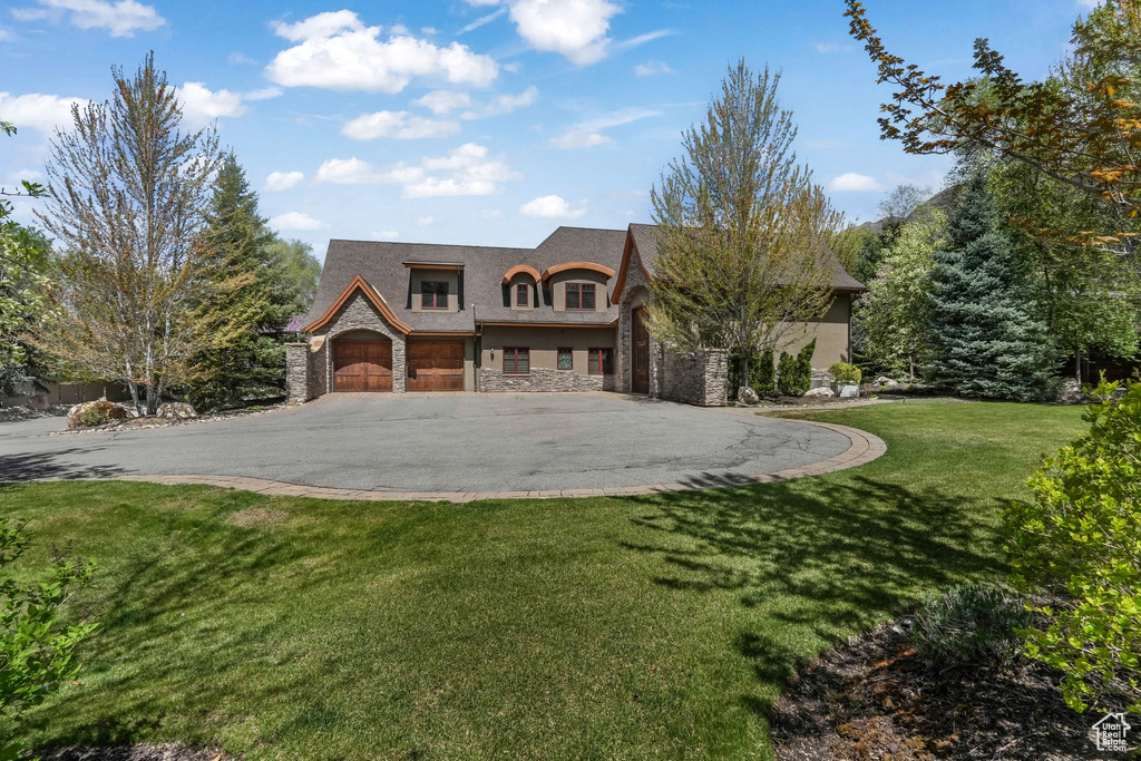 View of front of property with stone siding, driveway, a front yard, and a garage