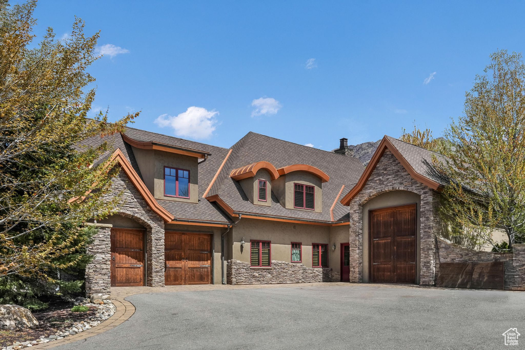 View of front of property with stone siding, stucco siding, asphalt driveway, roof with shingles, and a chimney