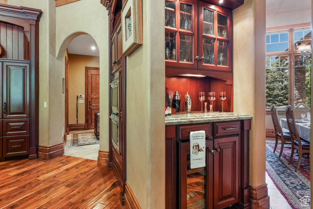Indoor dry bar featuring wine cooler, arched walkways, light wood-style floors, baseboards, and a towering ceiling