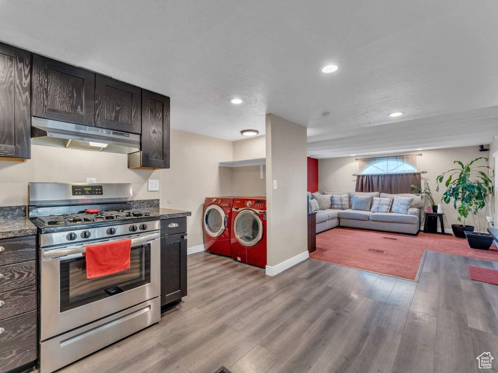 Kitchen with under cabinet range hood, stainless steel range with gas cooktop, separate washer and dryer, light wood finished floors, and recessed lighting