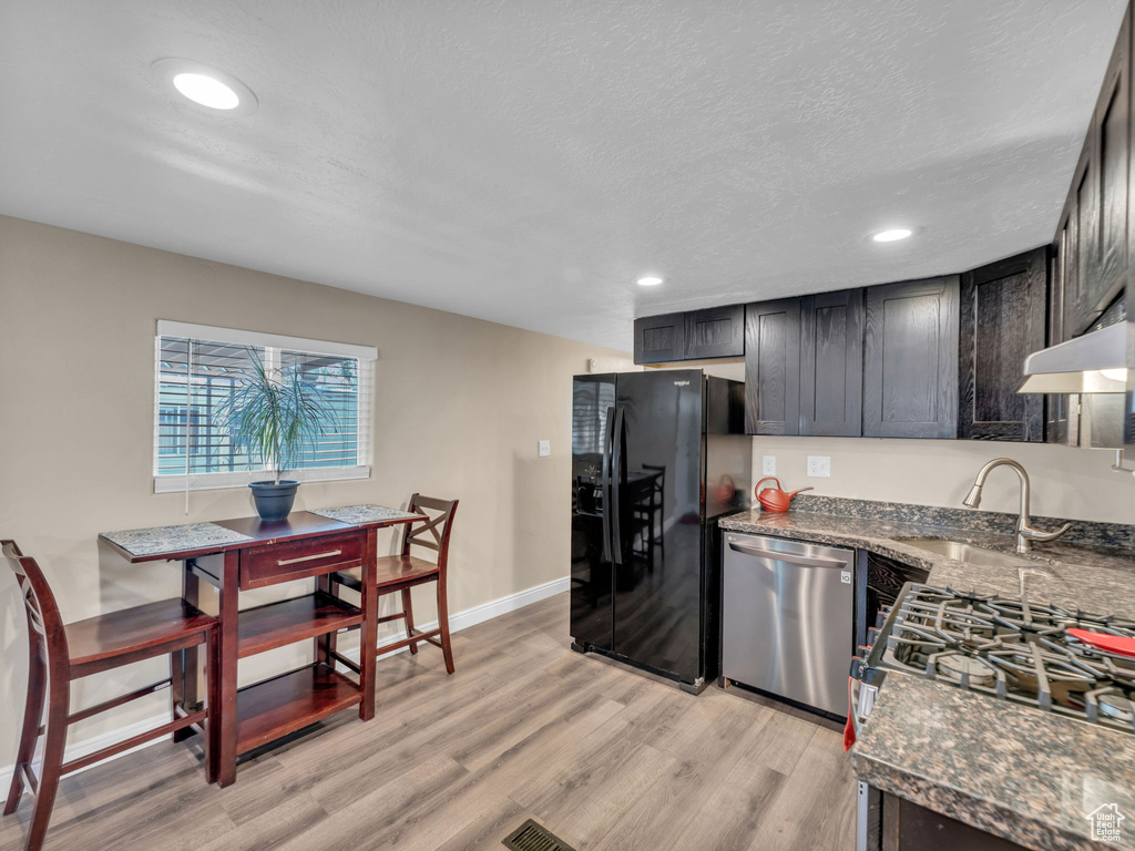Kitchen with appliances with stainless steel finishes, a sink, light wood-style floors, under cabinet range hood, and dark stone counters