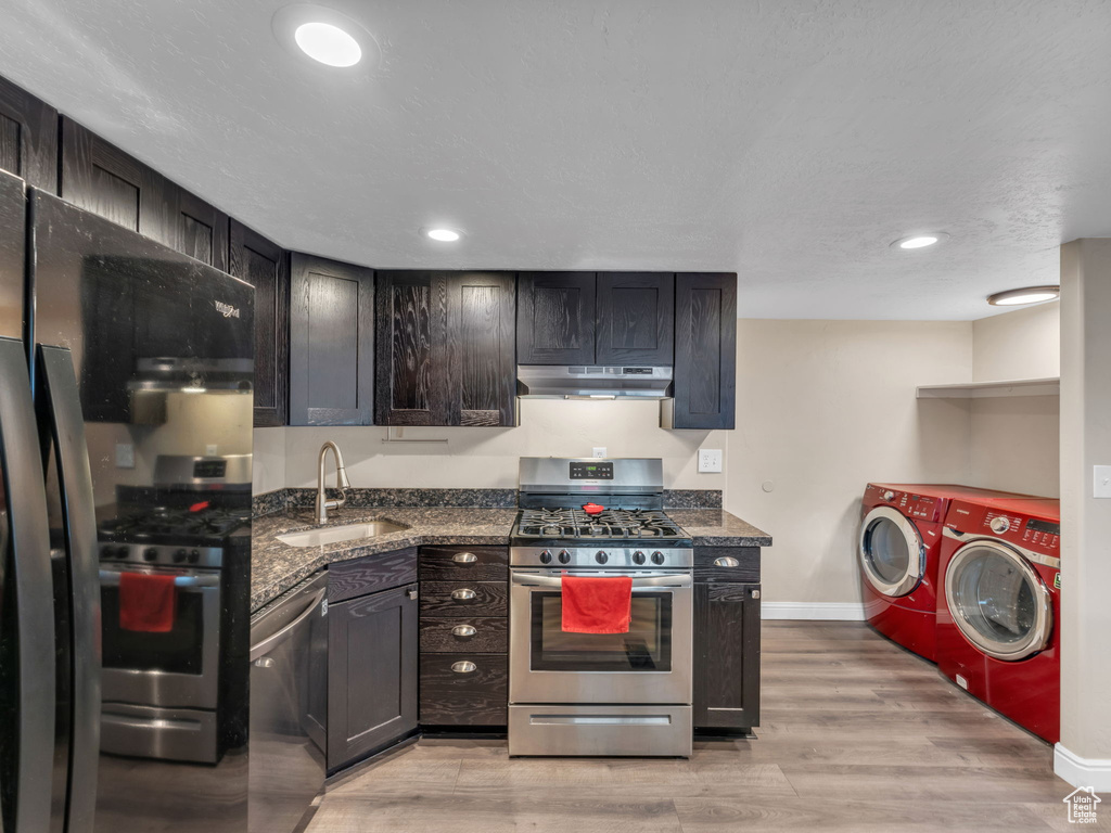 Kitchen with stainless steel appliances, a sink, independent washer and dryer, under cabinet range hood, and dark stone countertops