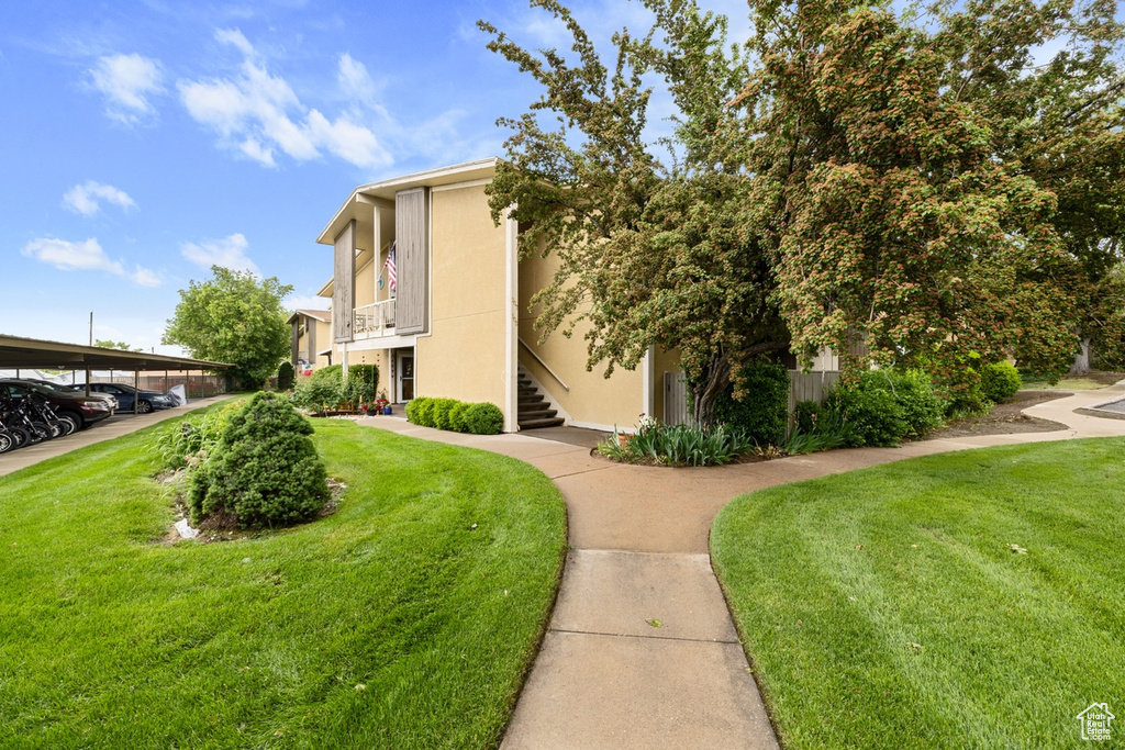View of side of home with a yard, stucco siding, covered parking, and stairs