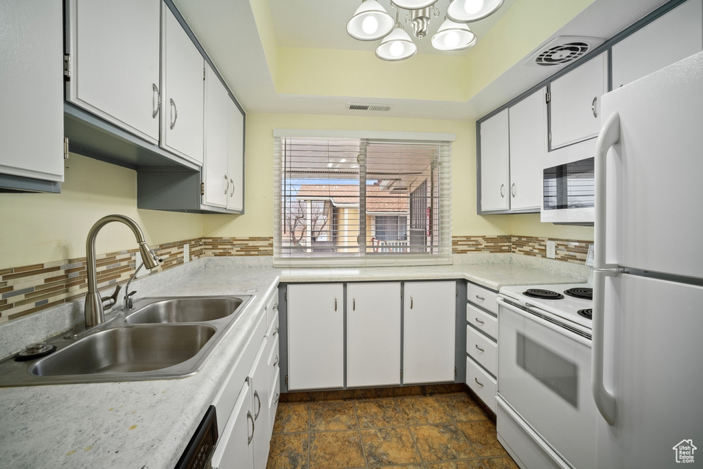 Kitchen featuring white appliances, a sink, a chandelier, light countertops, and white cabinetry