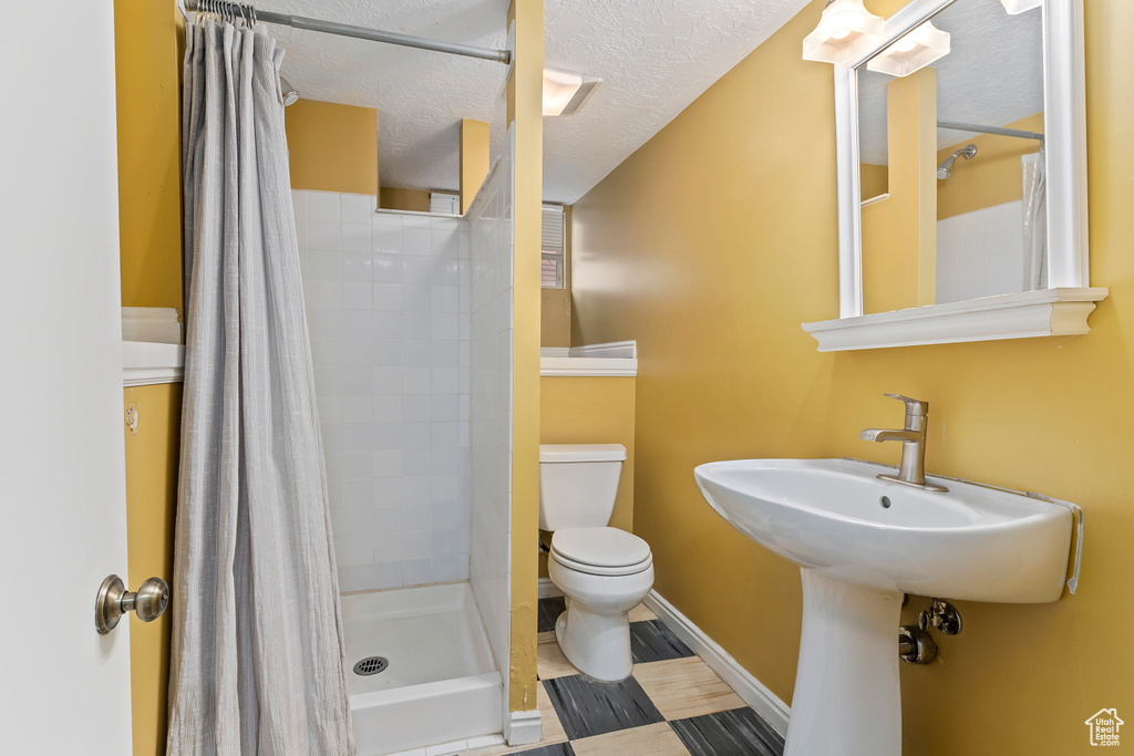 Bathroom featuring toilet, a stall shower, a textured ceiling, and baseboards