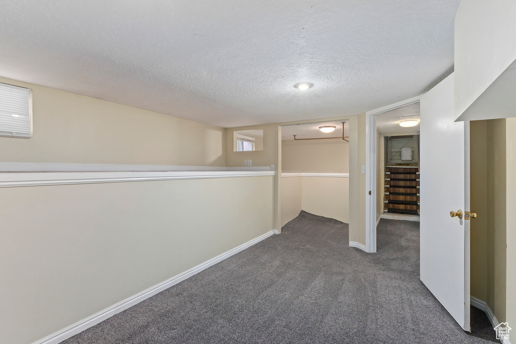 Finished basement featuring dark carpet, a textured ceiling, stairway, and baseboards