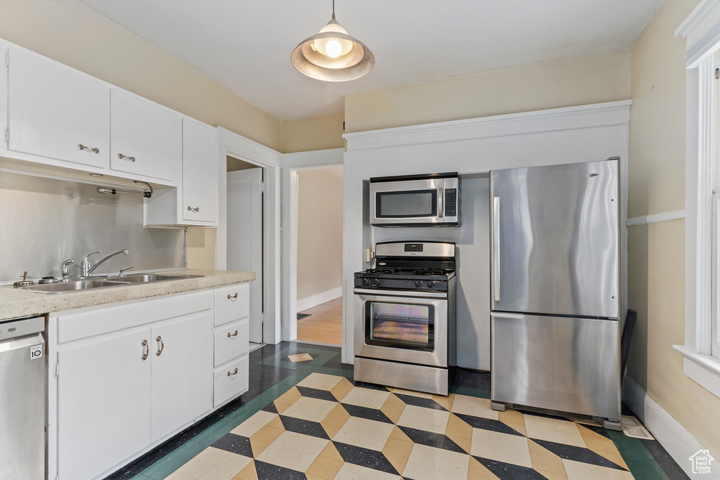 Kitchen with appliances with stainless steel finishes, a sink, light countertops, white cabinetry, and baseboards