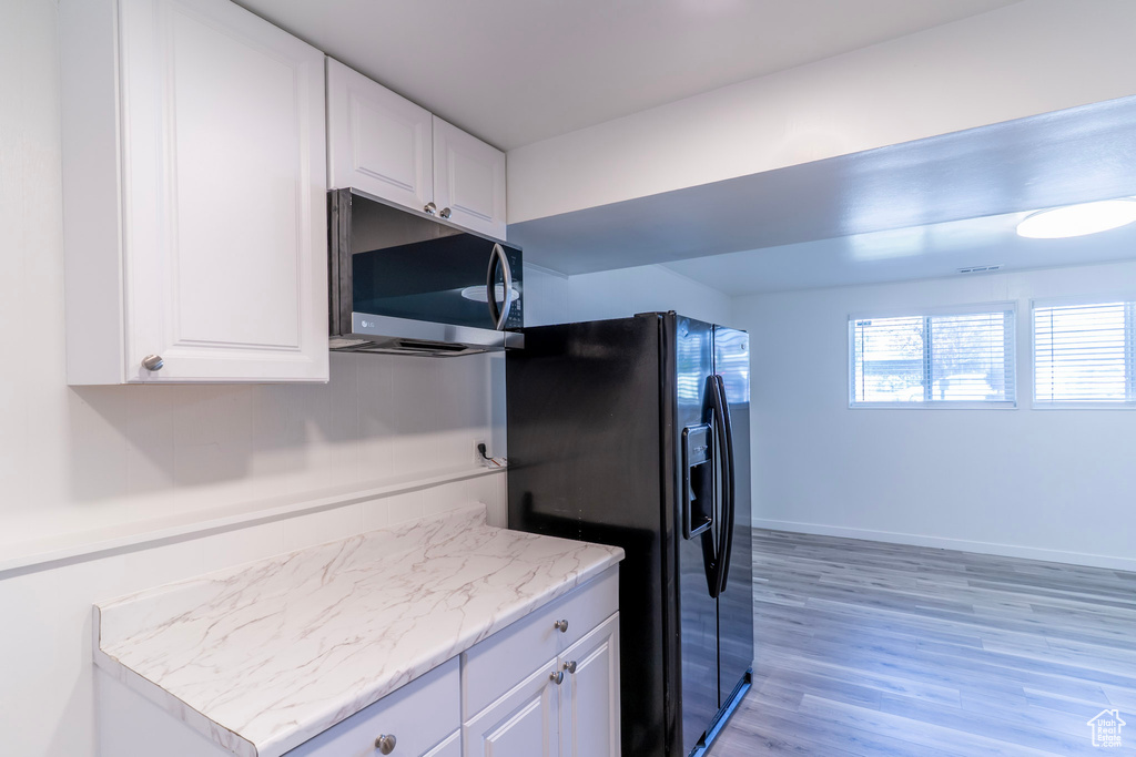 Kitchen featuring stainless steel microwave, black fridge, white cabinetry, light wood-style flooring, and light stone countertops