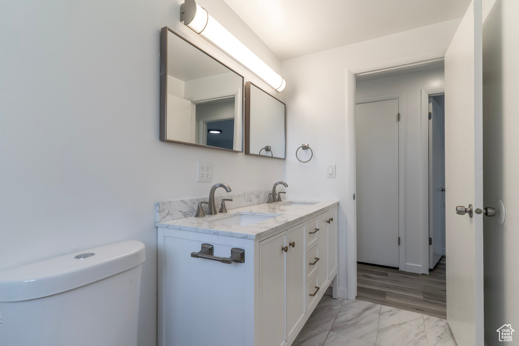 Bathroom featuring marble look tile flooring, double vanity, and toilet