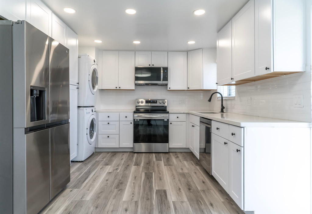 Kitchen with appliances with stainless steel finishes, stacked washer and clothes dryer, a sink, light countertops, and light wood-type flooring