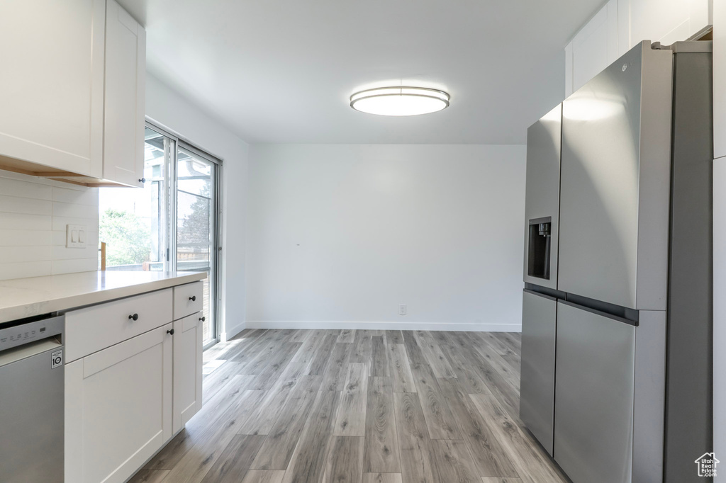 Kitchen featuring stainless steel appliances, white cabinets, light wood-type flooring, backsplash, and baseboards