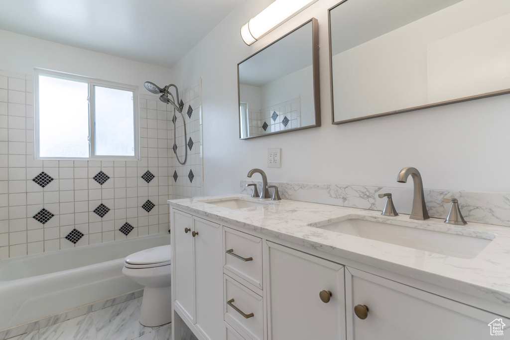 Full bath with toilet, double vanity, marble finish floors, and bathing tub / shower combination