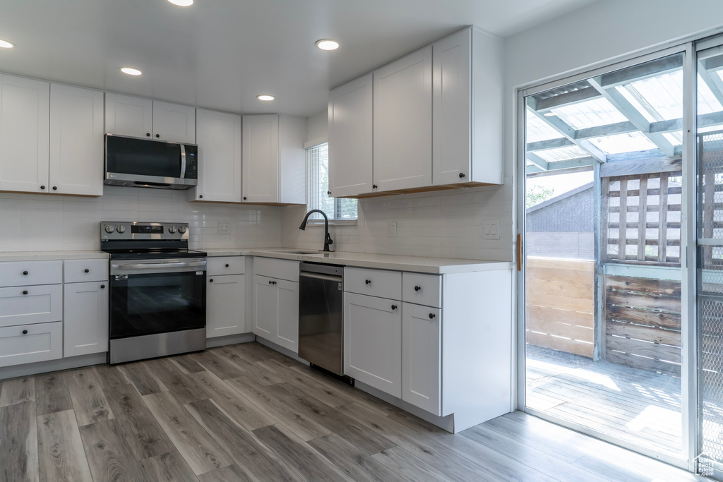 Kitchen with appliances with stainless steel finishes, light wood-style floors, decorative backsplash, light countertops, and recessed lighting