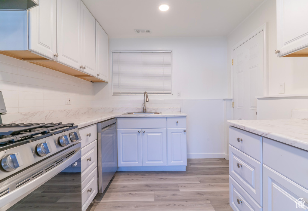 Kitchen with a sink, appliances with stainless steel finishes, white cabinetry, light wood-style floors, and recessed lighting
