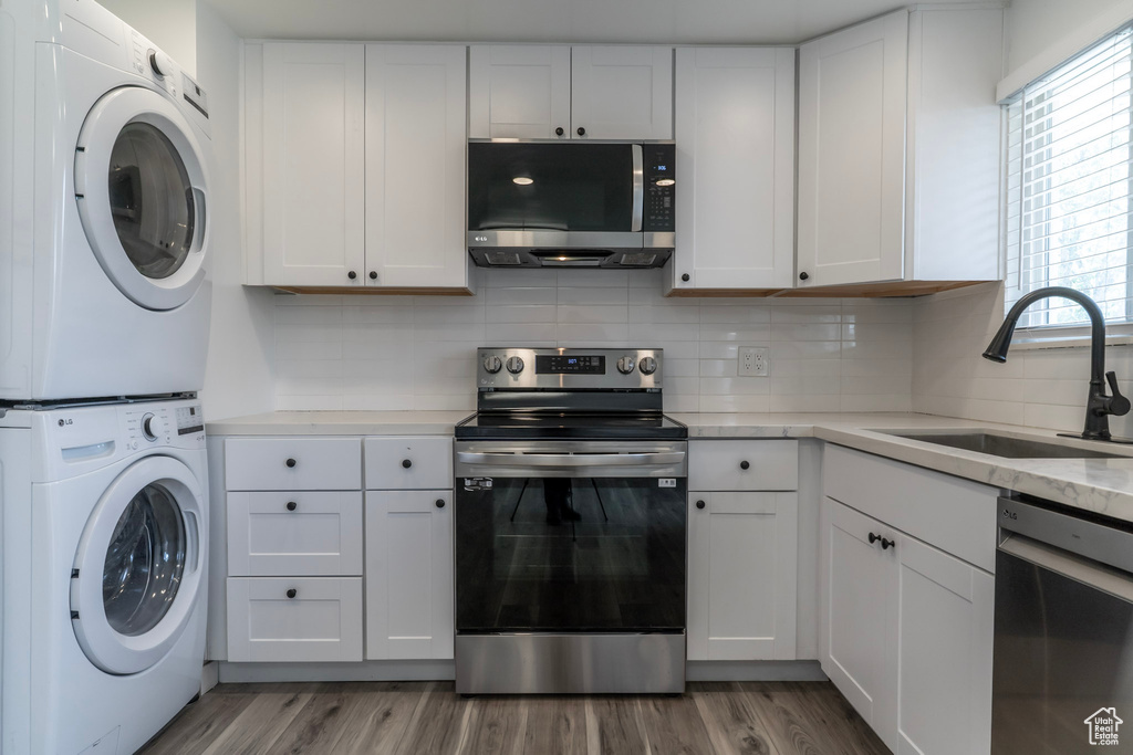 Kitchen featuring stainless steel appliances, a sink, stacked washer and clothes dryer, white cabinets, and tasteful backsplash