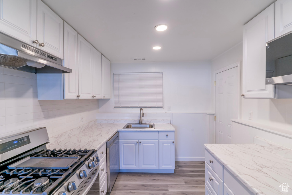Kitchen featuring stainless steel appliances, a sink, under cabinet range hood, light wood-type flooring, and white cabinetry
