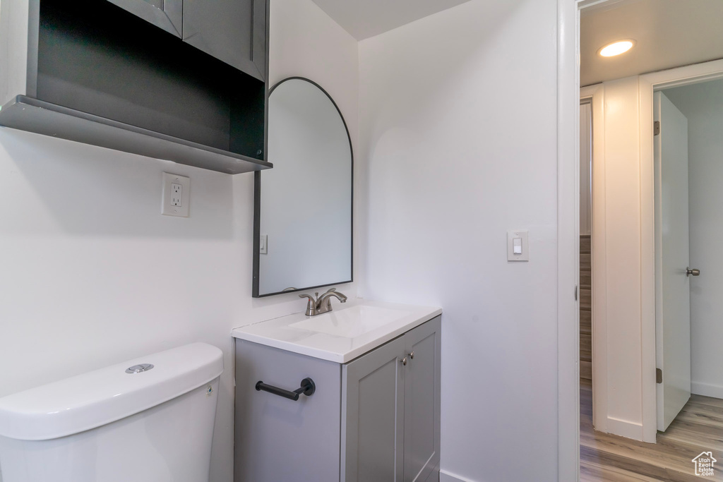 Half bath featuring wood finished floors, vanity, toilet, baseboards, and recessed lighting