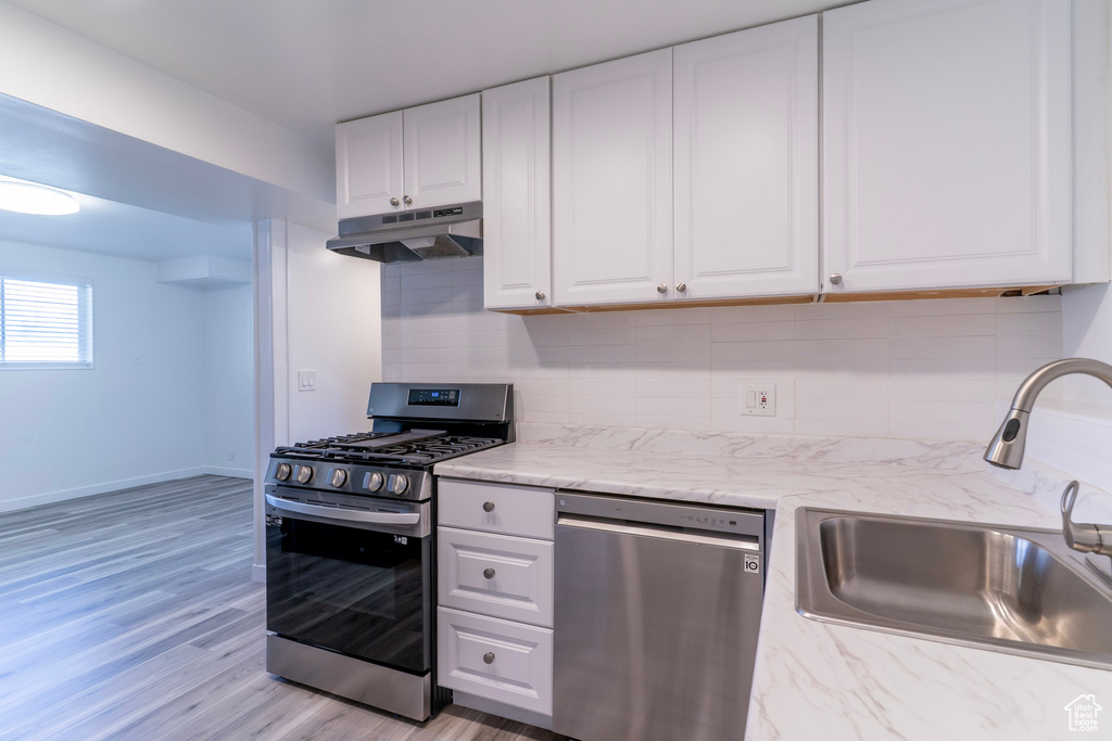 Kitchen with stainless steel appliances, a sink, under cabinet range hood, white cabinetry, and decorative backsplash