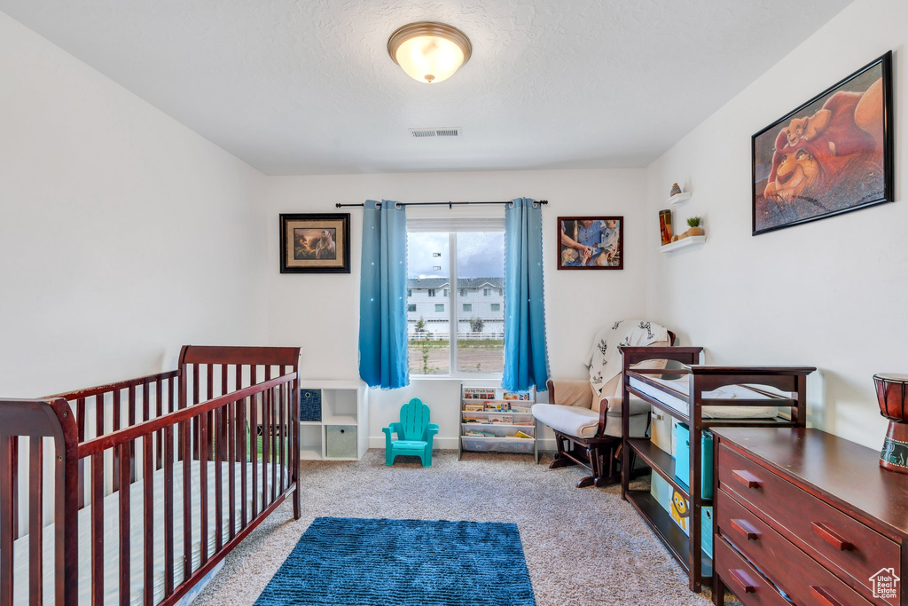 Bedroom with carpet floors, a textured ceiling, and a crib