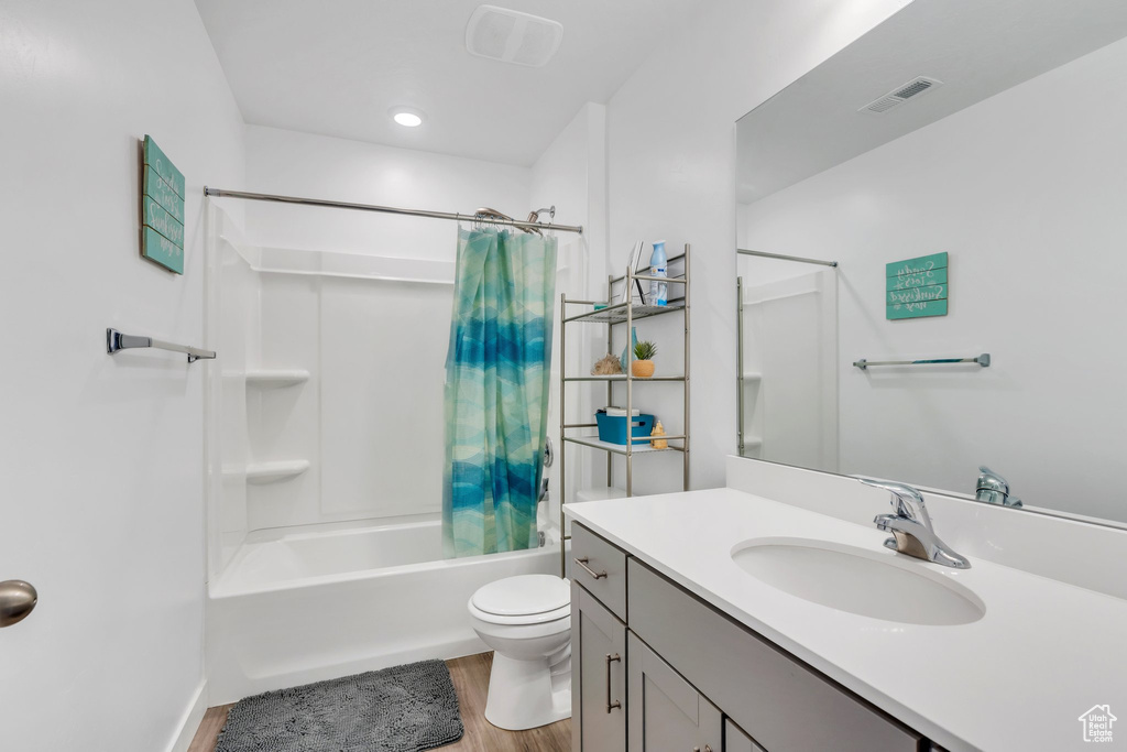 Full bathroom with wood finished floors, toilet, shower / bath combo with shower curtain, and vanity