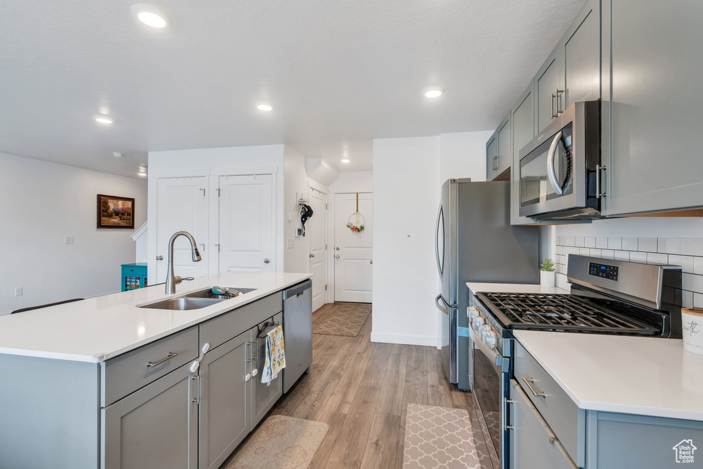 Kitchen with appliances with stainless steel finishes, a sink, gray cabinets, light wood finished floors, and recessed lighting