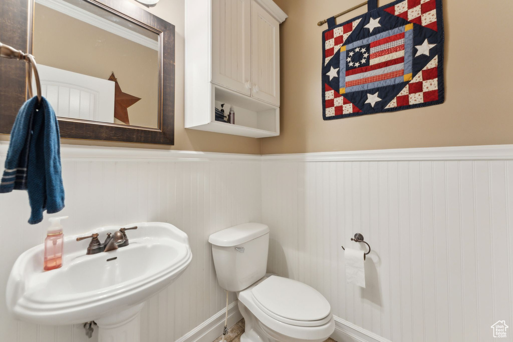 Bathroom with a wainscoted wall, a sink, toilet, and baseboards