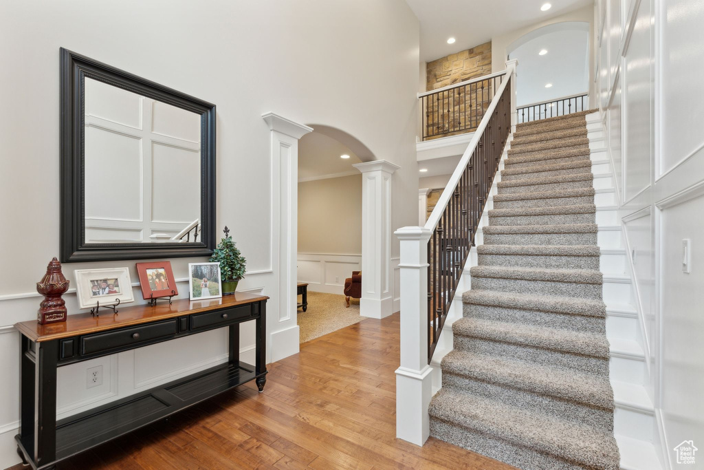 Stairs featuring ornate columns, arched walkways, wood finished floors, a decorative wall, and recessed lighting
