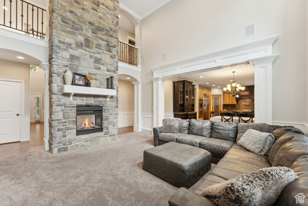 Living area with a high ceiling, a chandelier, a fireplace, ornamental molding, and ornate columns