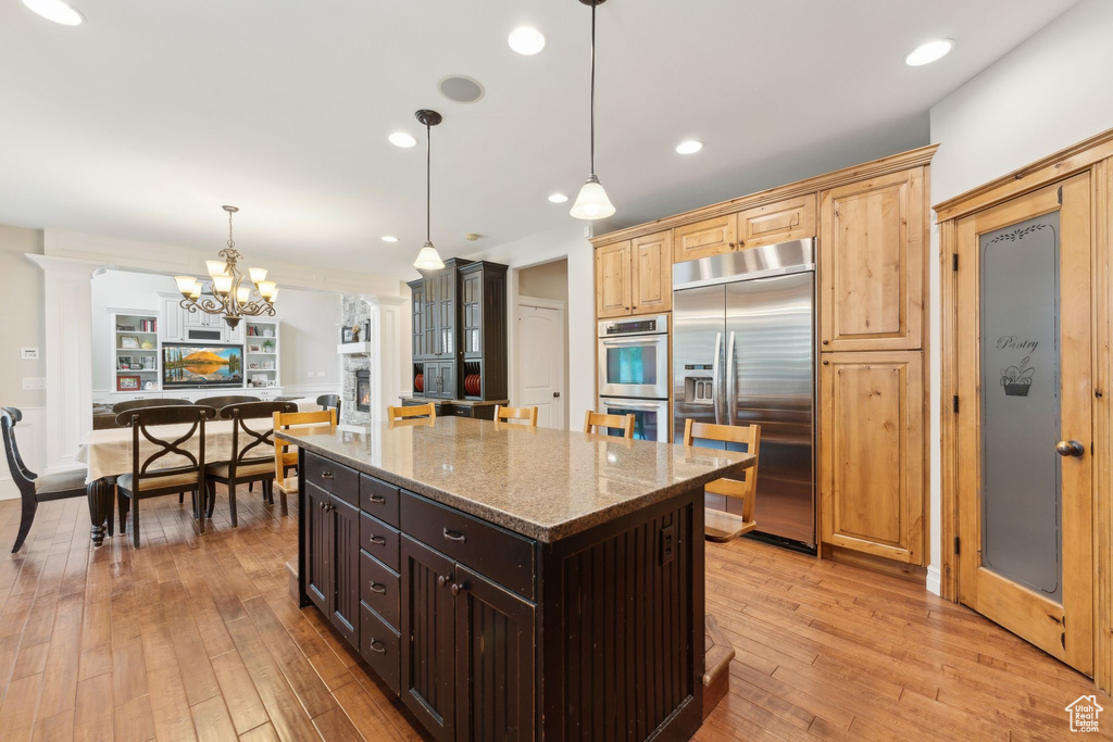 Kitchen with stainless steel appliances, light stone counters, a chandelier, light wood-style floors, and a center island