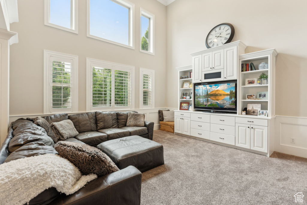 Living area with wainscoting, a high ceiling, healthy amount of natural light, light colored carpet, and a decorative wall