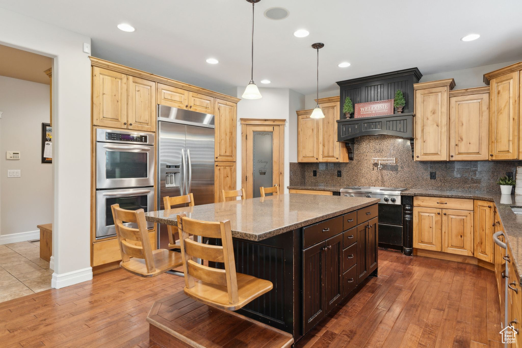 Kitchen featuring stainless steel appliances, a kitchen island, dark stone countertops, wood-type flooring, and tasteful backsplash