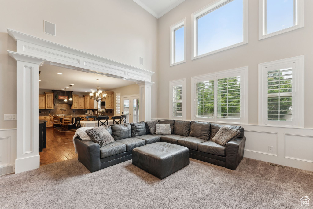 Carpeted living room with decorative columns, a chandelier, a towering ceiling, a wainscoted wall, and crown molding