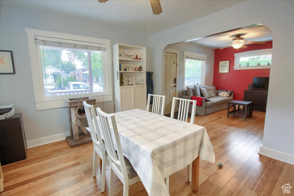 Dining area featuring ceiling fan, arched walkways, light wood-style floors, and baseboards