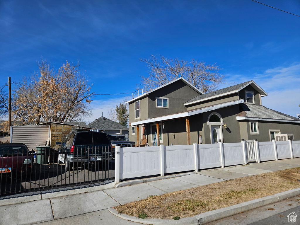 View of front of property featuring a fenced front yard, stucco siding, covered porch, and roof with shingles