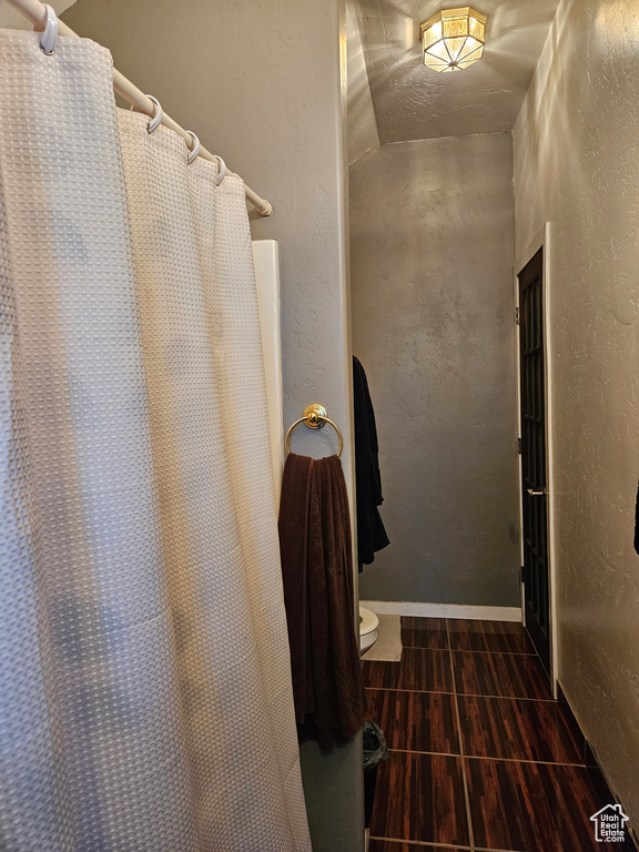 Full bath featuring toilet, a textured wall, tile patterned flooring, and curtained shower